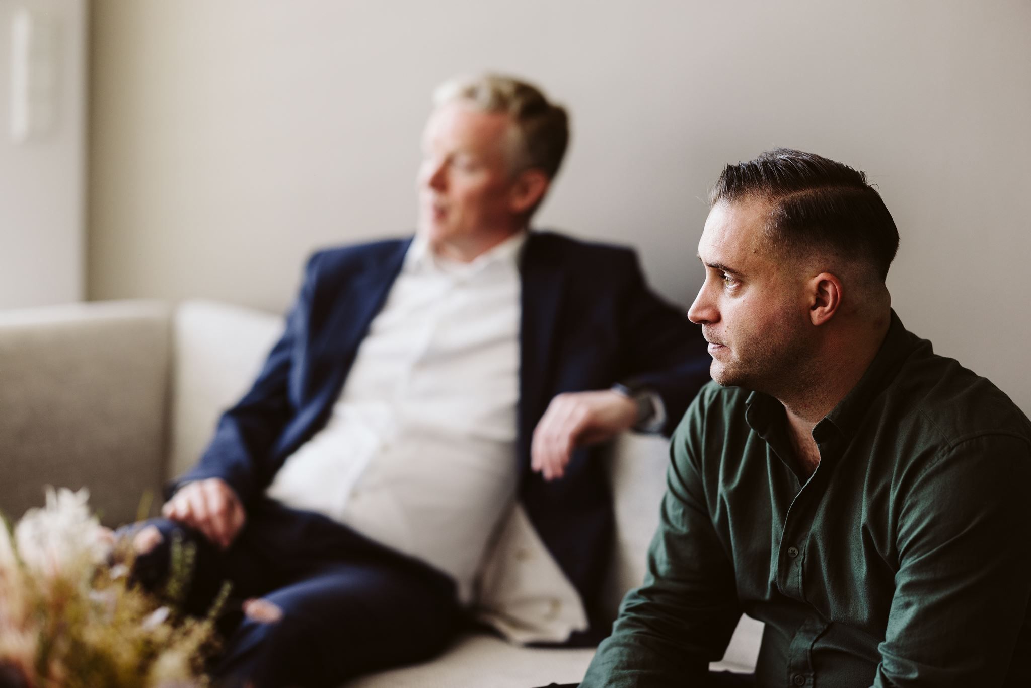 To menn sitter i en sofa i en uformell samtale, den ene i dress og den andre i grønn skjorte